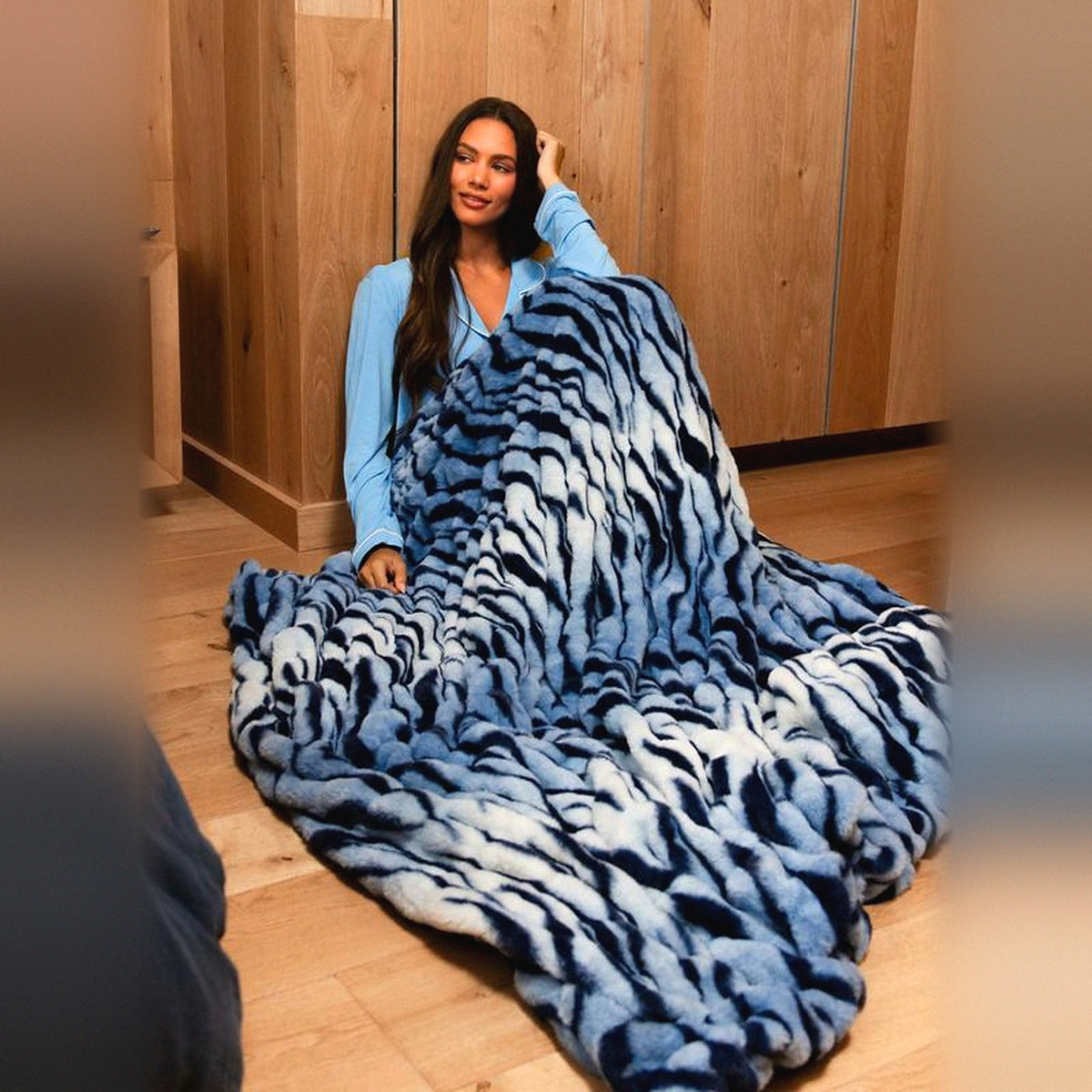 Mochi Mellow Cloud Throw in Blue Tiger — Blue tiger-print ruched faux-fur throw draped over a woman sitting on a wooden floor