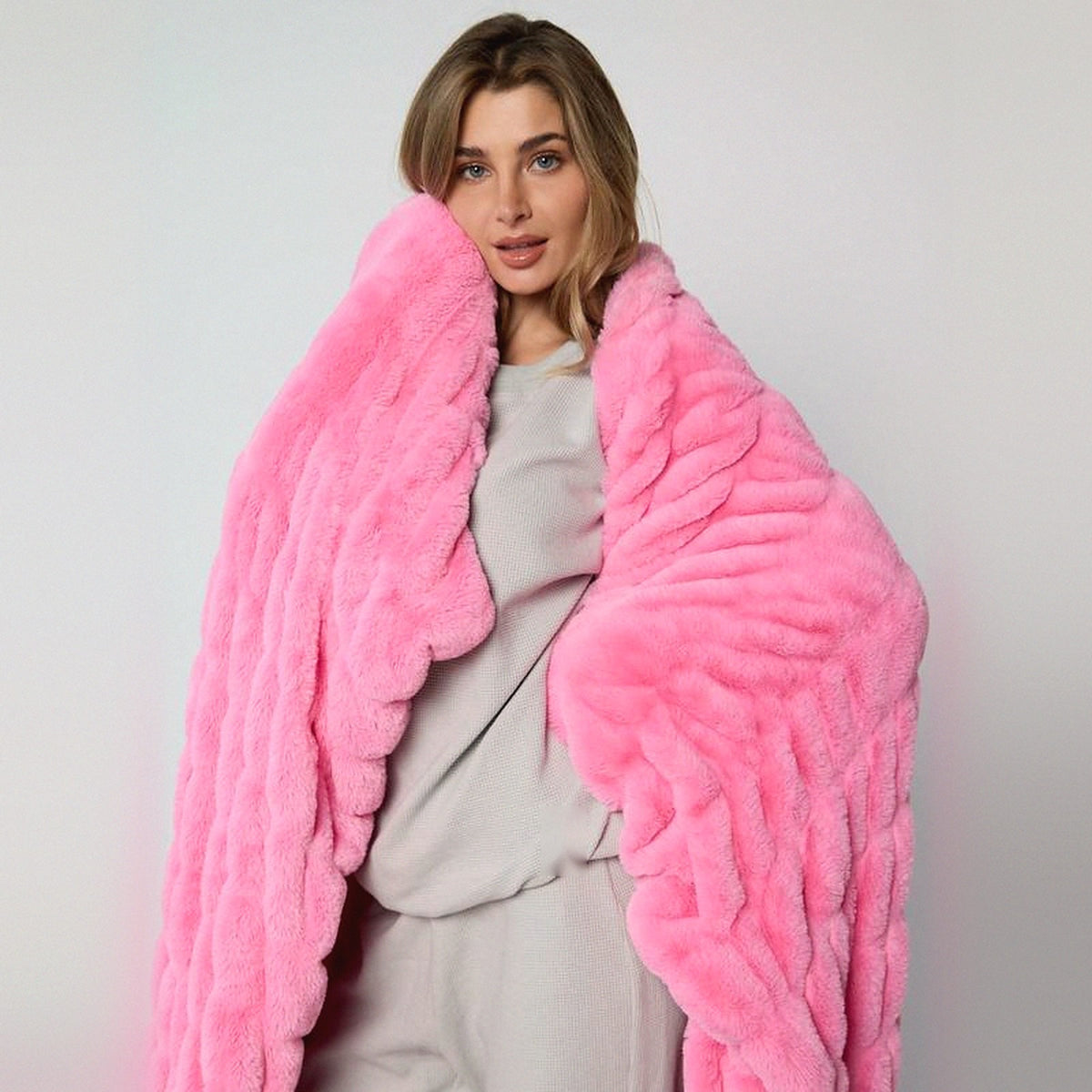 Mochi Mellow Cloud Throw in Bubblegum — Bubblegum pink ruched faux-fur throw held up around a woman's shoulders