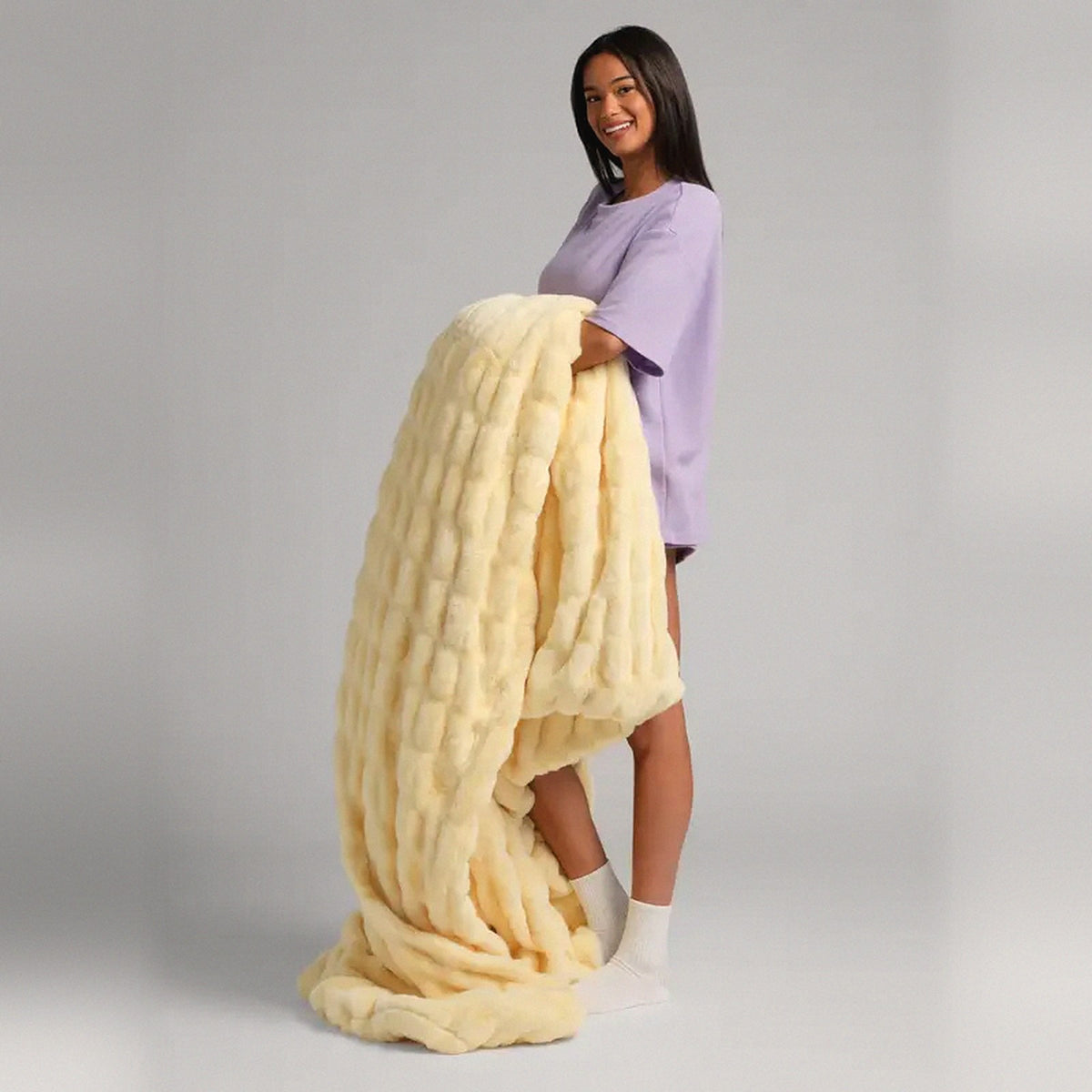Mochi Mellow Cloud Throw in Buttercream — Buttercream yellow ruched faux-fur throw held over a woman's arm, trailing to the floor
