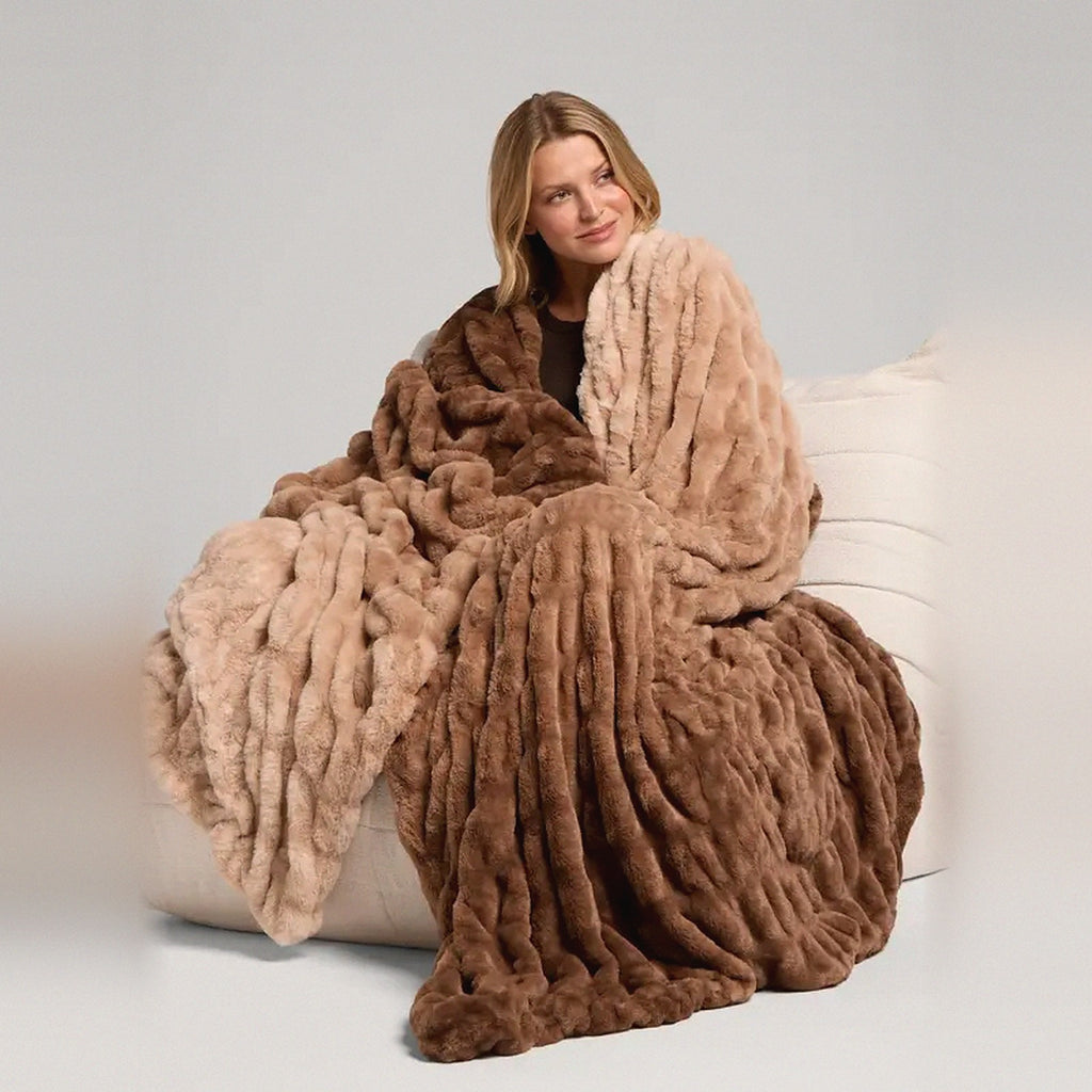 Mochi Mellow Cloud Throw in Caramel Ombré — Caramel ombré ruched faux-fur throw, two-tone brown and tan, wrapped around a woman on a cream lounger
