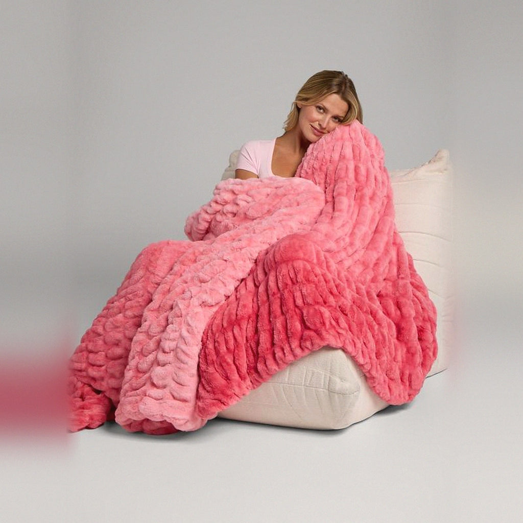Mochi Mellow Cloud Throw in Coral Pink — Coral pink two-tone ruched faux-fur throw draped over a woman on a cream lounger
