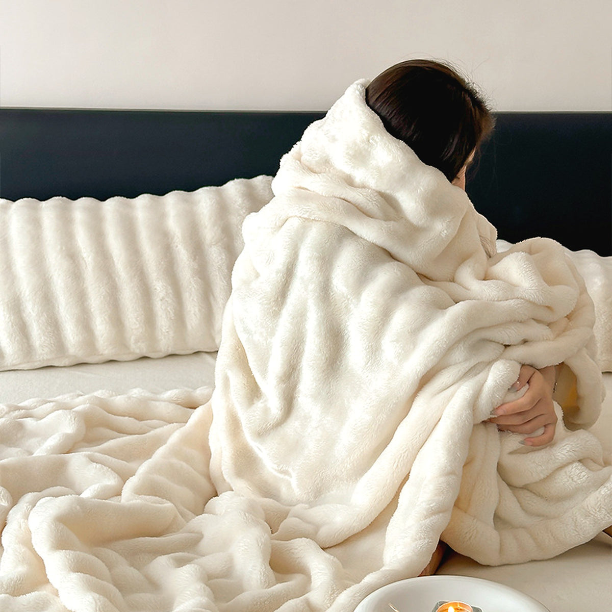 Mochi Mellow Cloud Throw in Frost — Frost white ruched faux-fur throw wrapped around a woman sitting on a bed