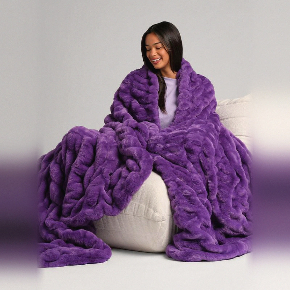 Mochi Mellow Cloud Throw in Grape — Grape purple ruched faux-fur throw wrapped around a woman on a cream lounger