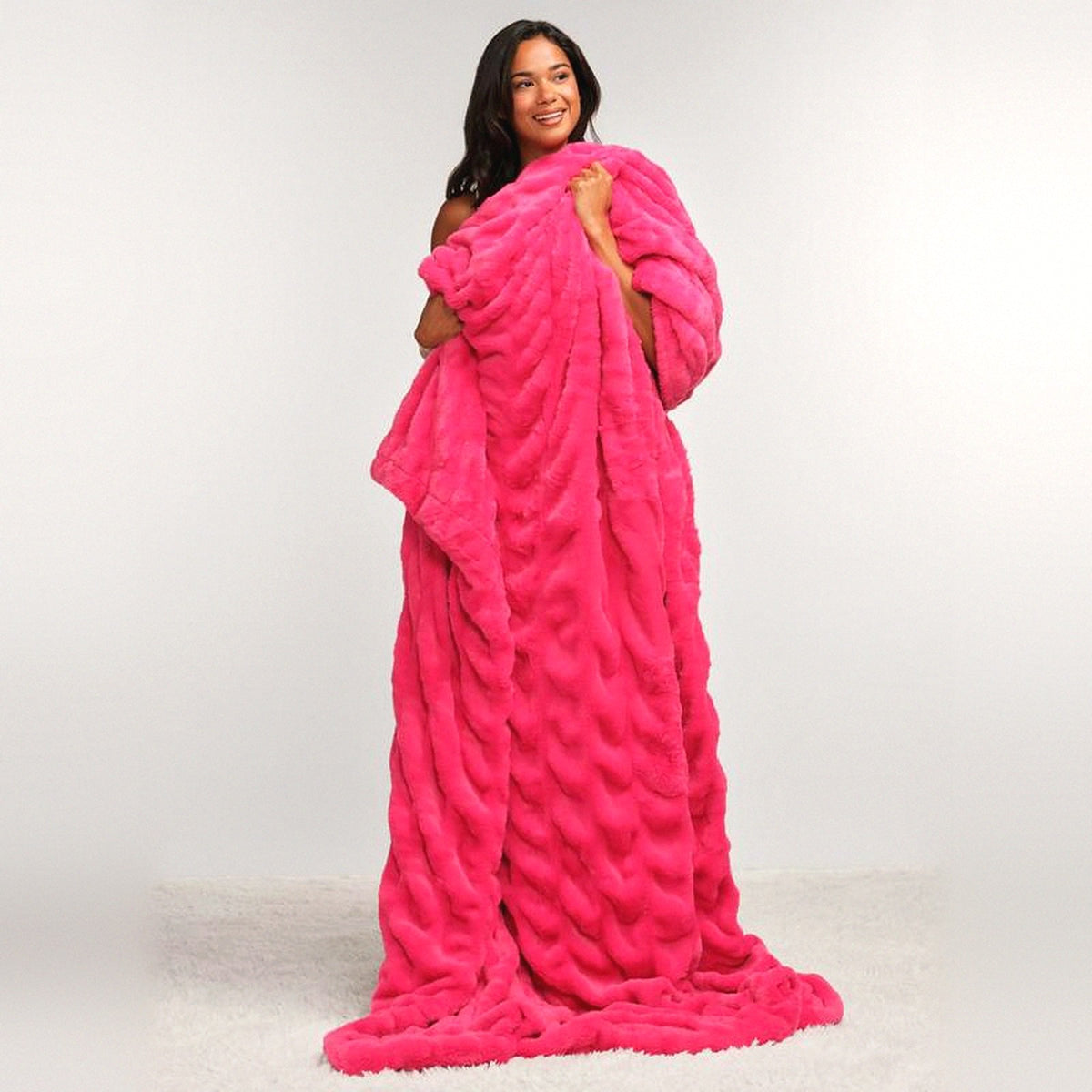 Mochi Mellow Cloud Throw in Hot Pink — Hot pink ruched faux-fur throw wrapped around a woman, pooling on a white rug