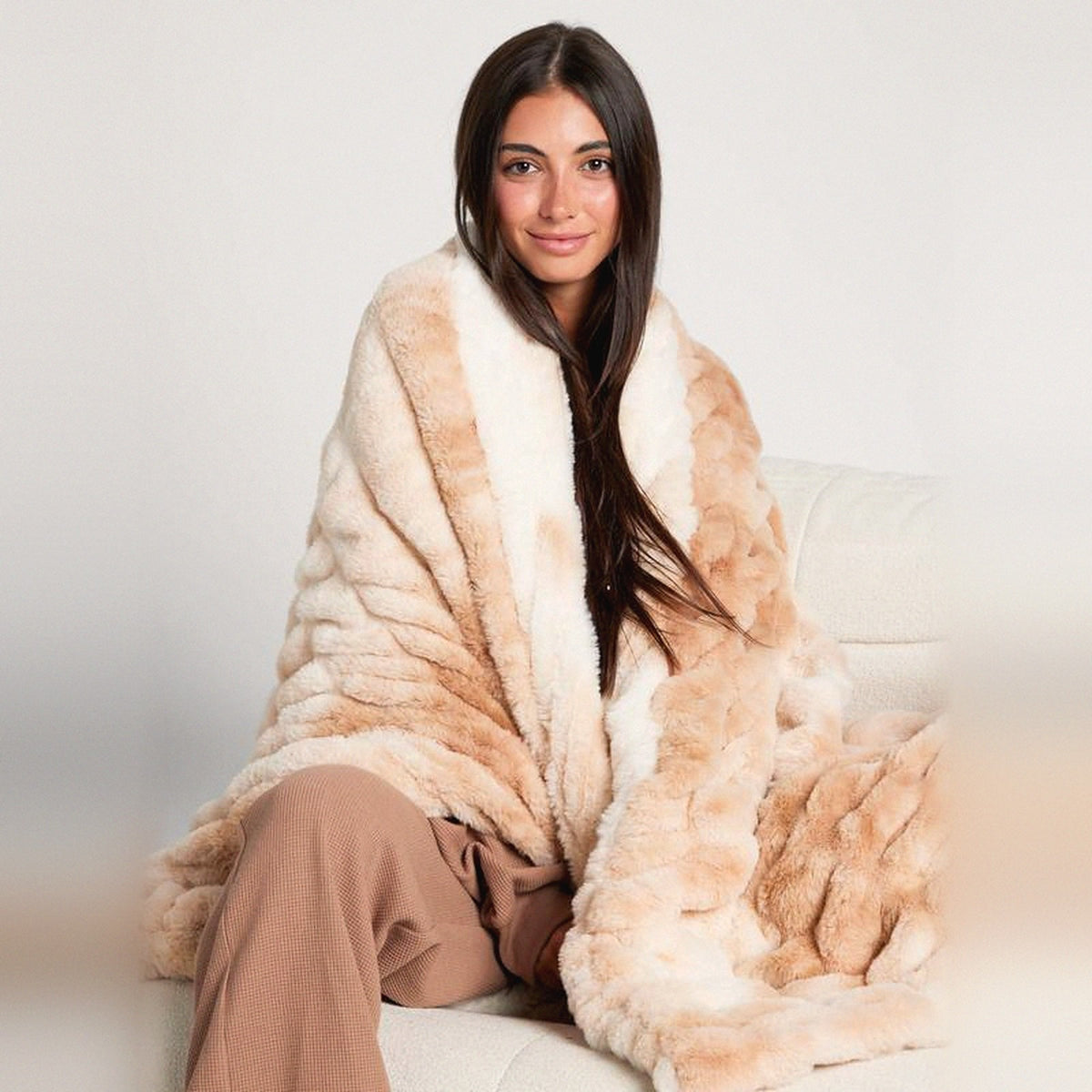 Mochi Mellow Cloud Throw in Latte — Latte ruched faux-fur throw wrapped around a woman on a cream sofa