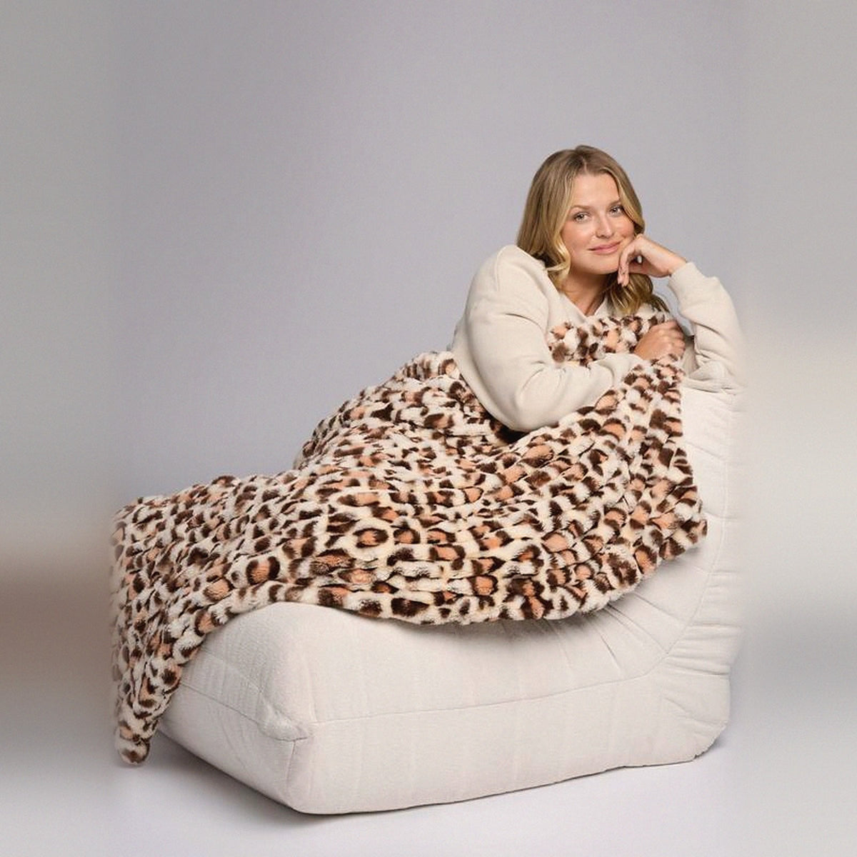 Mochi Mellow Cloud Throw in Leopard — Leopard-print ruched faux-fur throw over a woman on a cream lounger