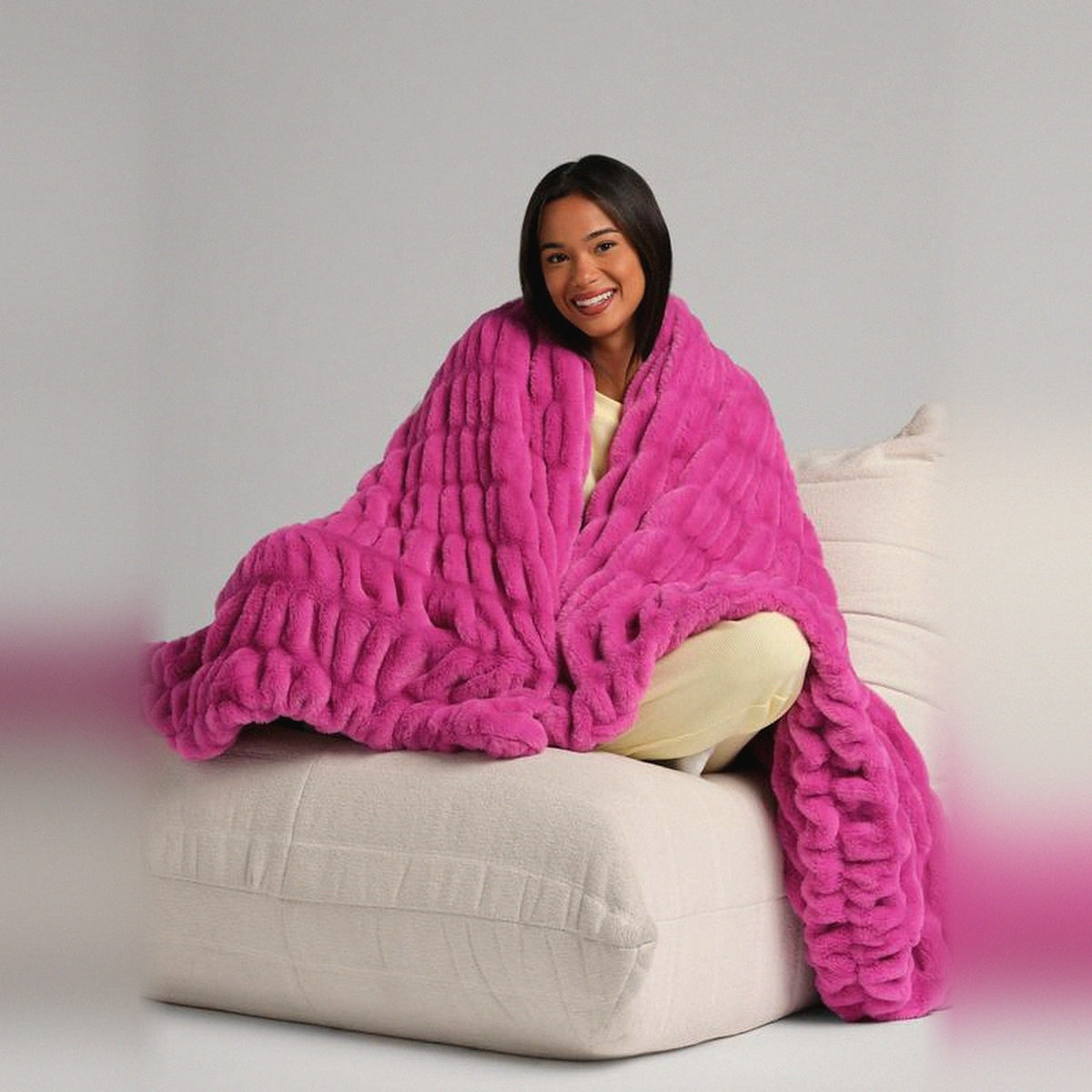 Mochi Mellow Cloud Throw in Magenta — Magenta ruched faux-fur throw wrapped around a woman sitting on a cream lounger
