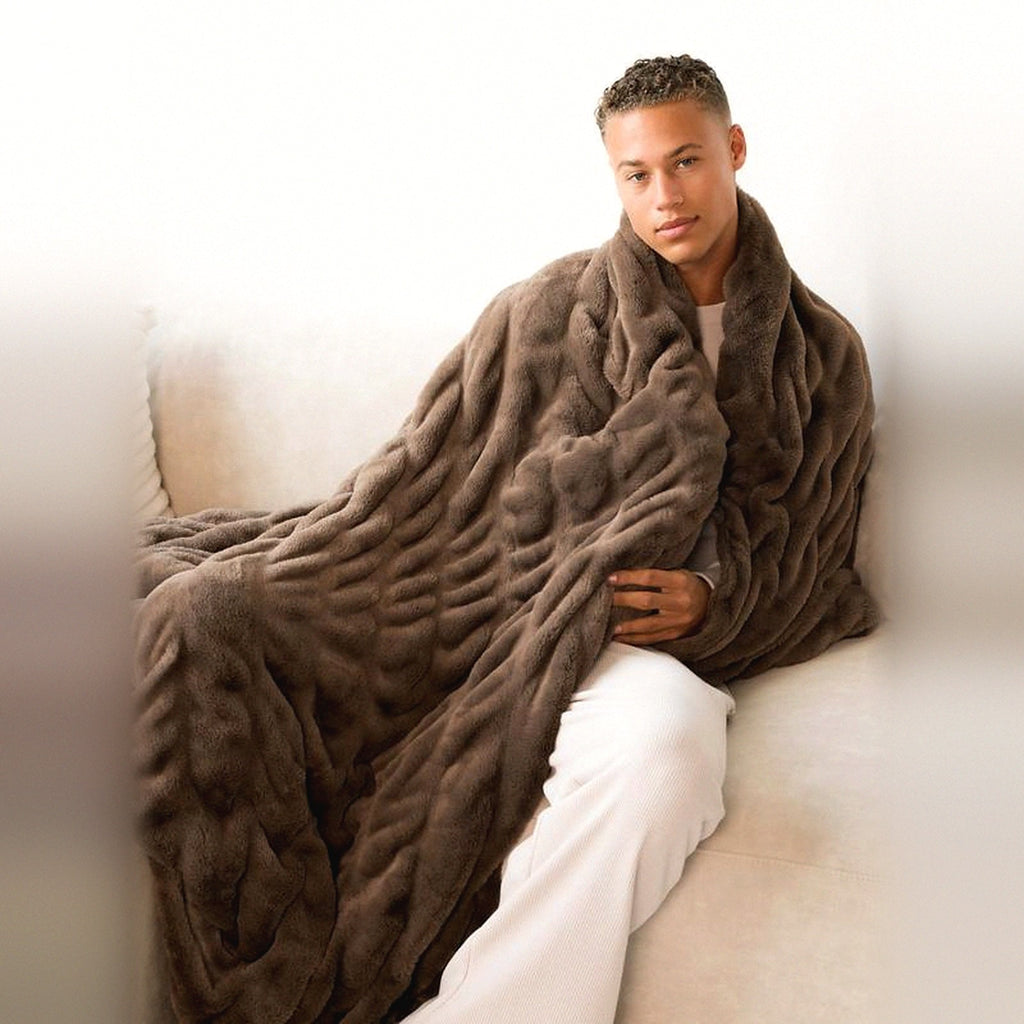 Mochi Mellow Cloud Throw in Mocha — Mocha brown ruched faux-fur throw wrapped around a man sitting on a cream sofa