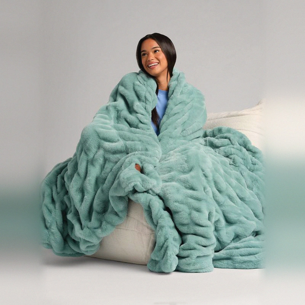Mochi Mellow Cloud Throw in Seafoam — Seafoam ruched faux-fur throw wrapped around a woman sitting on a cream lounger