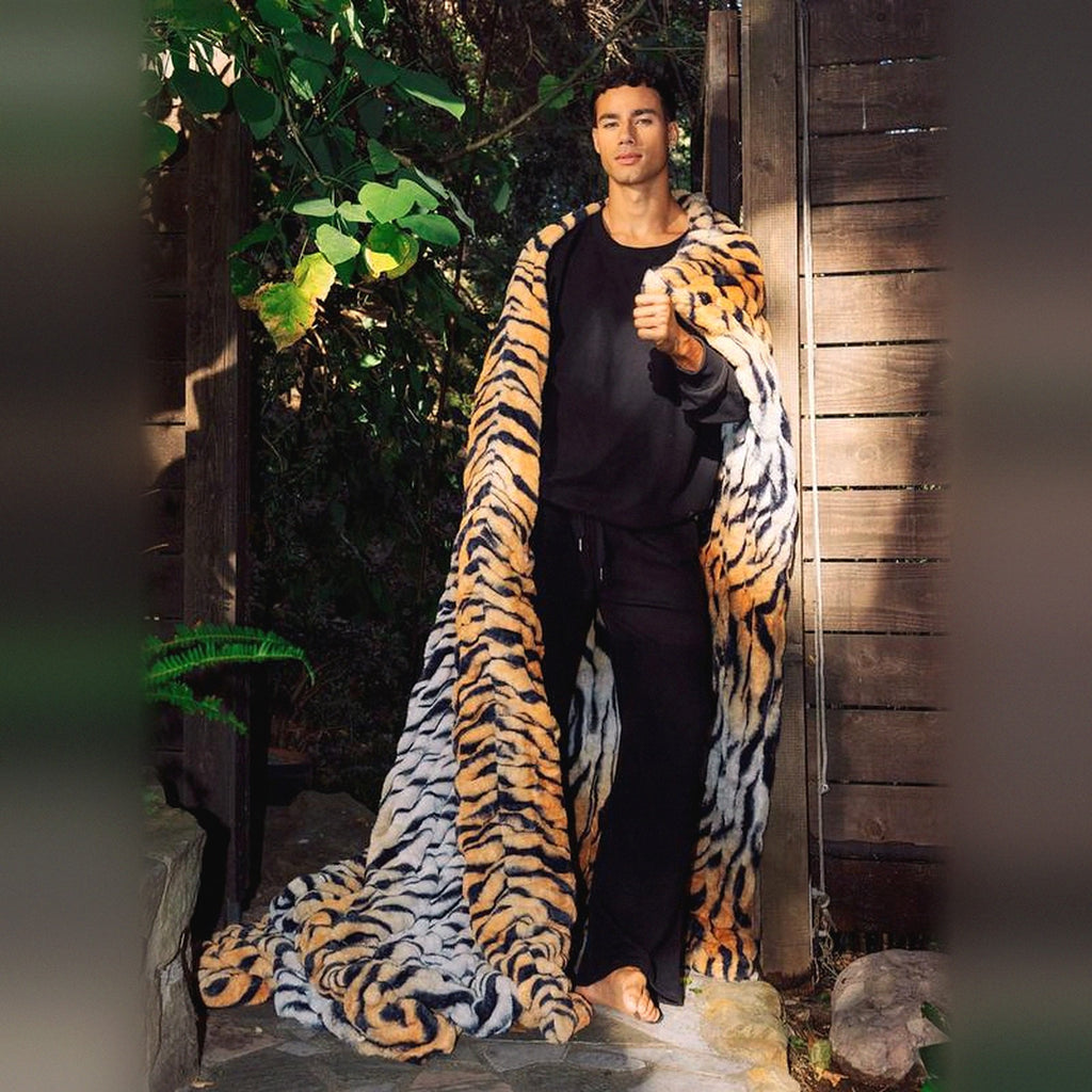 Mochi Mellow Cloud Throw in Tiger — Tiger-print ruched faux-fur throw draped over a man's shoulders in a garden